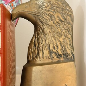May include: A brass eagle head sculpture, likely a bookend, with detailed feather texture and a strong beak. The sculpture has a rectangular base and is set against a neutral background. The eagle's head is angled slightly upward.