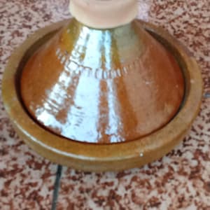 May include: A brown ceramic tagine pot with a conical lid and a circular base. The tagine is a traditional North African cooking vessel, often used for slow-cooked stews and braises. The pot is made of earthenware.
