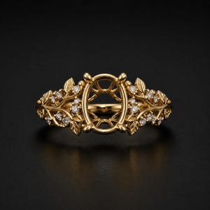Puede incluir: Un anillo de oro con un engaste central ovalado diseñado para una piedra preciosa. La banda está elaborada con un intrincado trabajo de metal que recuerda a ramas y hojas, acentuado con pequeñas piedras redondas y claras incrustadas.