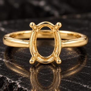 Peut inclure: Une bague en or jaune poli dotée d'un panier central de forme ovale avec quatre griffes conçues pour maintenir une pierre précieuse. L'anneau est lisse et arrondi, présentant une finition métallique réfléchissante sur tout le bijou.