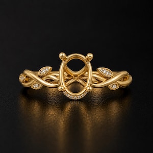 May include: A yellow gold ring setting featuring an oval-shaped center mount with four prongs. The band is designed with intertwined vine-like metalwork, accented with small, clear pavé-set stones along the leaves and the base of the center mount.