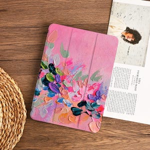 Può includere: Una custodia rettangolare per tablet caratterizzata da un design a pittura a olio testurizzata in stile impasto, con uno sfondo rosa e vivaci pennellate spesse nei toni del blu, viola, arancione, verde e bianco, con design a tre pieghe.