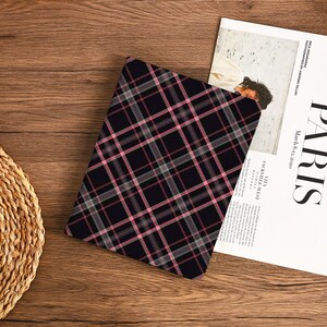 Può includere: Una custodia per tablet con motivo a quadri neri e rosa. La custodia presenta un motivo ripetuto di linee rosa e bianche su sfondo nero. Una rivista con la parola "PARIS" è parzialmente visibile.