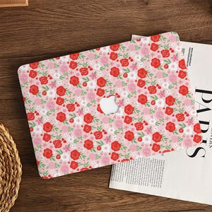 Puede incluir: Una funda para portátil con un estampado floral de rosas rojas y rosas y hojas verdes sobre un fondo rosa claro. La funda tiene un recorte para el logotipo de Apple.