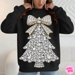 May include: Black sweatshirt featuring a sparkling Christmas tree design. The tree is adorned with numerous clear, faceted gems and topped with a gold bow. The design is centered on the front of the sweatshirt.