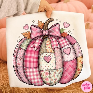 Pode incluir: Uma almofada decorativa branca com um design de abóbora patchwork rosa. A abóbora tem um caule castanho, um laço xadrez rosa e várias secções com padrões rosa e florais. Corações e estrelas acentuam o design.