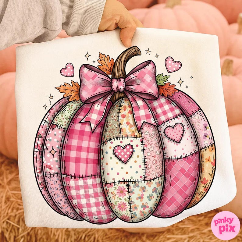 May include: A white decorative pillow featuring a pink patchwork pumpkin design. The pumpkin has a brown stem, a pink gingham bow, and various pink and floral patterned sections. Hearts and stars accent the design.