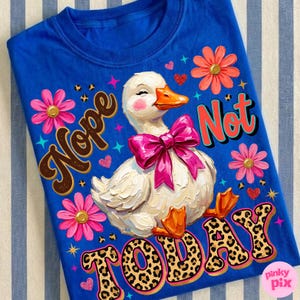 May include: A blue t-shirt featuring a white duck with a pink bow, orange beak and feet, and rosy cheeks. The shirt has the words "Nope Not Today" in a mix of fonts and colors, with floral and heart accents.