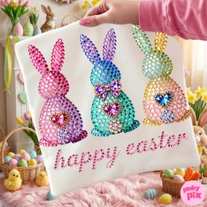 May include: White Easter-themed pillowcase featuring three rhinestone-studded bunny rabbits in pink, blue, and yellow. Each bunny has a heart-shaped gem. The words "happy easter" are written in pink rhinestones.