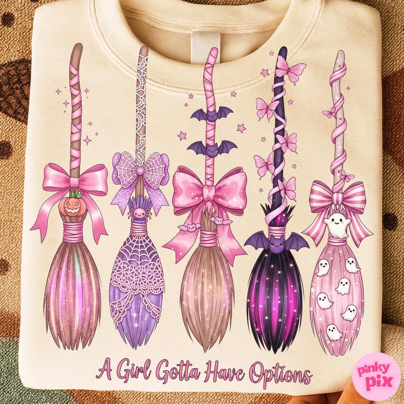 May include: Cream-colored sweatshirt featuring five decorative witch brooms in shades of pink, purple, and brown. Each broom has unique embellishments, including bows, bats, spiders, and ghosts. The text "A Girl Gotta Have Options" is printed at the bottom.