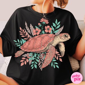 May include: Black t-shirt with a pink sea turtle and floral design. The turtle is surrounded by pink and green flowers and leaves.