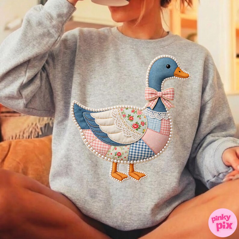 K&ouml;nnte beinhalten: Ein graues Sweatshirt mit einem Patchwork-G&auml;nsemotiv. Die Gans hat einen blauen Kopf, eine rosa Schleife und einen K&ouml;rper aus verschiedenen gemusterten Stoffen, darunter Blumenmuster und Vichy. Das Design ist mit wei&szlig;en Perlen umrandet.