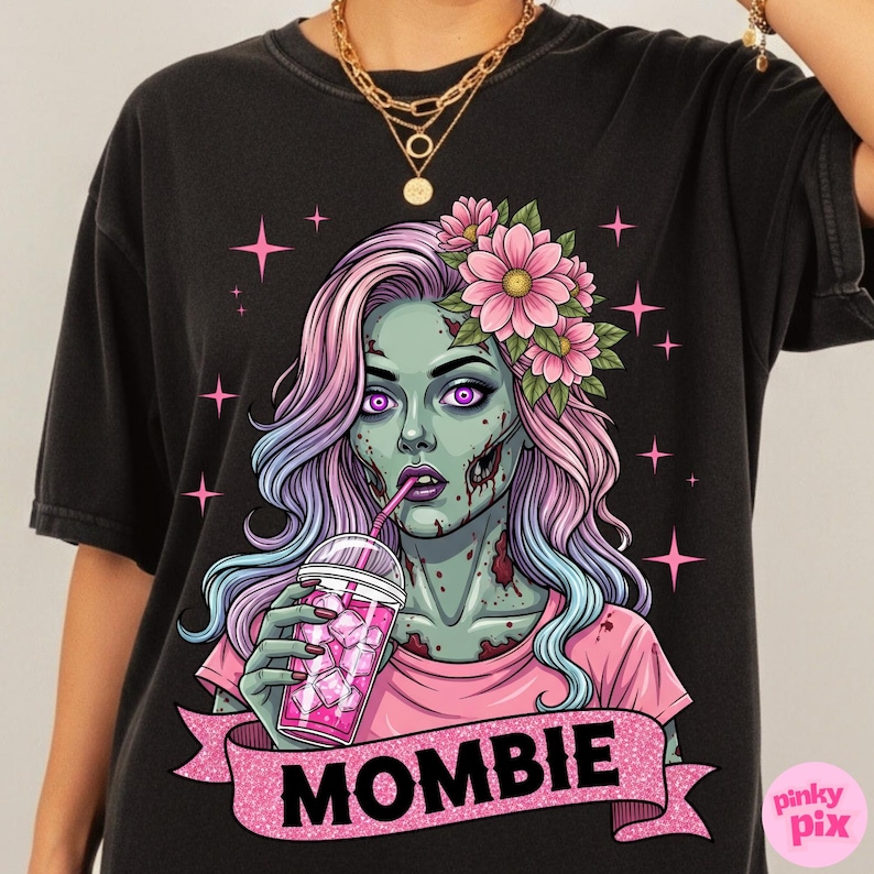 May include: Black t-shirt featuring a zombie illustration with pink and purple hair, flowers, and a drink. The zombie has green skin and the word "MOMBIE" on a pink banner.