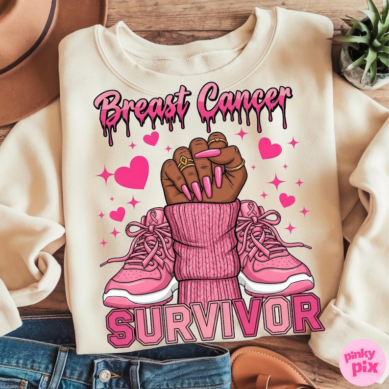 May include: Cream-colored sweatshirt with the words "Breast Cancer Survivor" in pink. The graphic features a raised fist with long pink nails, pink hearts, and pink sneakers. The design includes pink ribbons.