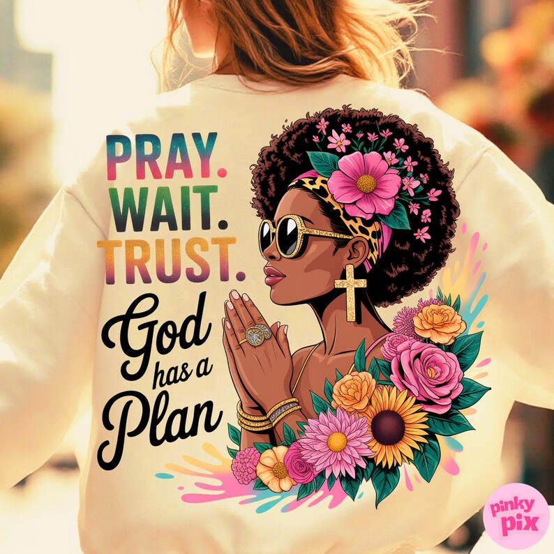 May include: Cream-colored sweatshirt featuring a graphic of a woman with sunglasses, a floral head wrap, and gold cross earrings. The text "PRAY. WAIT. TRUST. God has a Plan" is printed on the back, along with colorful flowers.