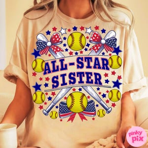 May include: A beige t-shirt with a softball-themed graphic. The design features yellow softballs, crossed baseball bats, and red, white, and blue bows and stars. The text "ALL-STAR SISTER" is prominently displayed in blue.