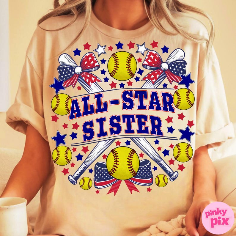 May include: A beige t-shirt with a softball-themed graphic. The design features yellow softballs, crossed baseball bats, and red, white, and blue bows and stars. The text "ALL-STAR SISTER" is prominently displayed in blue.