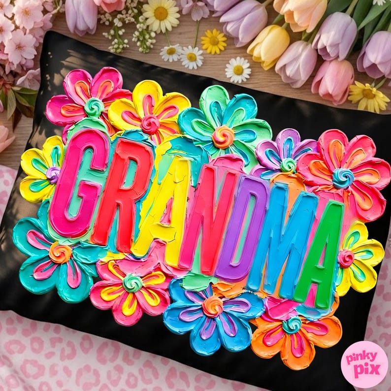 May include: Black pillow with the word "GRANDMA" in colorful, raised lettering, surrounded by vibrant, textured flowers in shades of pink, yellow, blue, and orange. The pillow has a textured appearance, suggesting a painted or embroidered design.