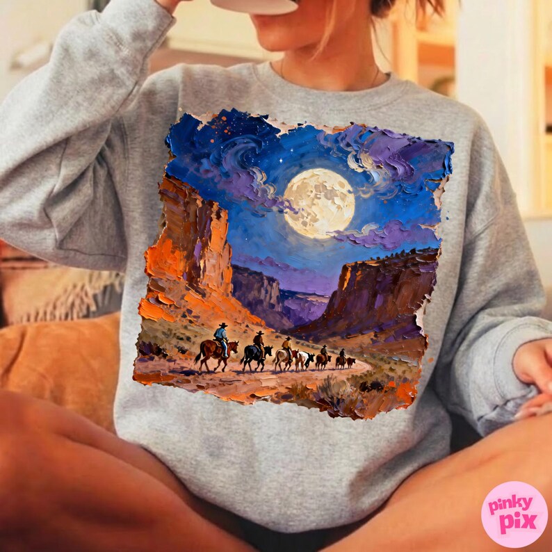 May include: A gray sweatshirt featuring a vibrant painting of a desert landscape under a full moon. The artwork depicts a group of riders on horseback traveling through a canyon, with a night sky filled with stars and clouds.