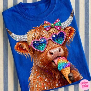 May include: A royal blue t-shirt featuring a rhinestone-studded Highland cow wearing heart-shaped sunglasses and a bow. The cow is licking a rainbow-colored ice cream cone. The image has a fun, whimsical theme.