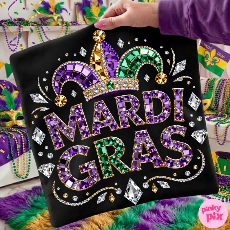 May include: Black pillow with the words "MARDI GRAS" in purple and green jewel-like letters. The pillow features a jeweled crown and diamond accents. The design is held by a person with a purple sleeve. The background includes Mardi Gras beads and decorations.