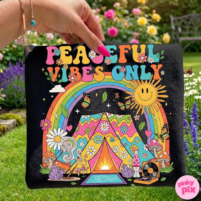 May include: Black graphic tee with the words "PEACEFUL VIBES ONLY" in colorful letters. The design includes a rainbow, butterflies, a smiling sun, a tent, mushrooms, and a record player. The tee is held up by a hand.