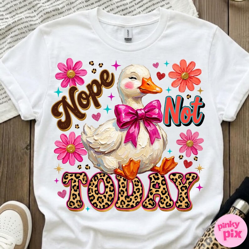 May include: White t-shirt with a graphic of a duck wearing a pink bow, surrounded by flowers and hearts. The words "Nope Not Today" are displayed in a playful font with leopard print accents. A fun, whimsical design.