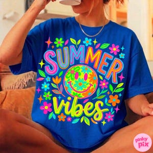 May include: A royal blue t-shirt with a vibrant graphic design. The design features the words "SUMMER VIBES" in a colorful, playful font, along with a smiley face and floral accents. The shirt is a casual, relaxed fit.