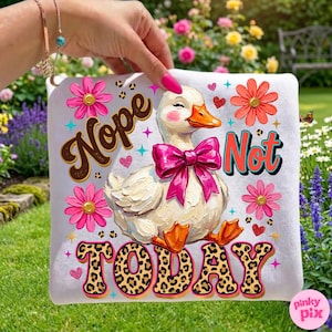 May include: White square pillow with a cartoon duck wearing a pink bow. The pillow has the words "Nope Not Today" in various fonts and colors, along with pink flowers and hearts. The duck has rosy cheeks and orange feet.