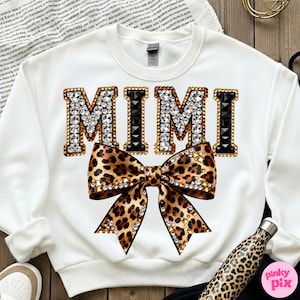 May include: White sweatshirt with the word "MIMI" in jeweled letters and a leopard print bow. The letters are outlined in gold and black, with clear and black rhinestones. A leopard print water bottle is visible.
