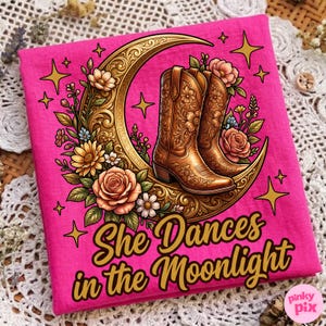 May include: A hot pink t-shirt featuring a graphic of brown cowboy boots on a gold crescent moon, surrounded by flowers and stars. The text "She Dances in the Moonlight" is written in gold script.