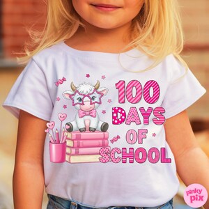 Pu&ograve; includere: Maglietta bianca con una mucca dei cartoni animati con occhiali a forma di stella e papillon, seduta su libri rosa. Il testo "100 Days of School" &egrave; rosa. Sono presenti anche un portapenne rosa e grafiche di caramelle.