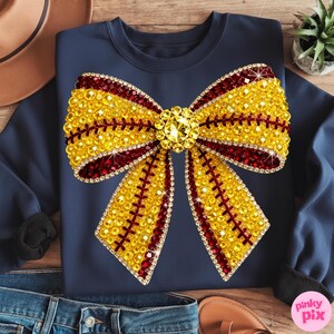 May include: Navy blue sweatshirt with a large, embellished bow design. The bow is predominantly yellow with red accents and sparkling rhinestones. The design is centered on the front of the sweatshirt, creating a striking visual effect.