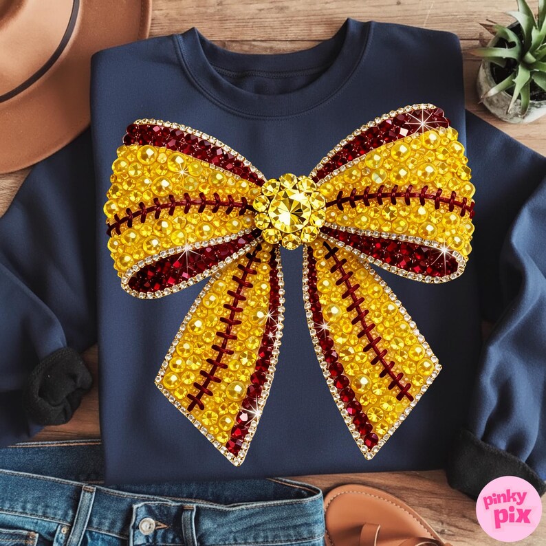 May include: Navy blue sweatshirt with a large, embellished bow design. The bow is predominantly yellow with red accents and sparkling rhinestones. The design is centered on the front of the sweatshirt, creating a striking visual effect.