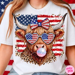 May include: White t-shirt featuring a Highland cow with patriotic sunglasses and a bow, all adorned with the American flag design. The cow is blowing a bubble, and the design includes a leopard print pattern.