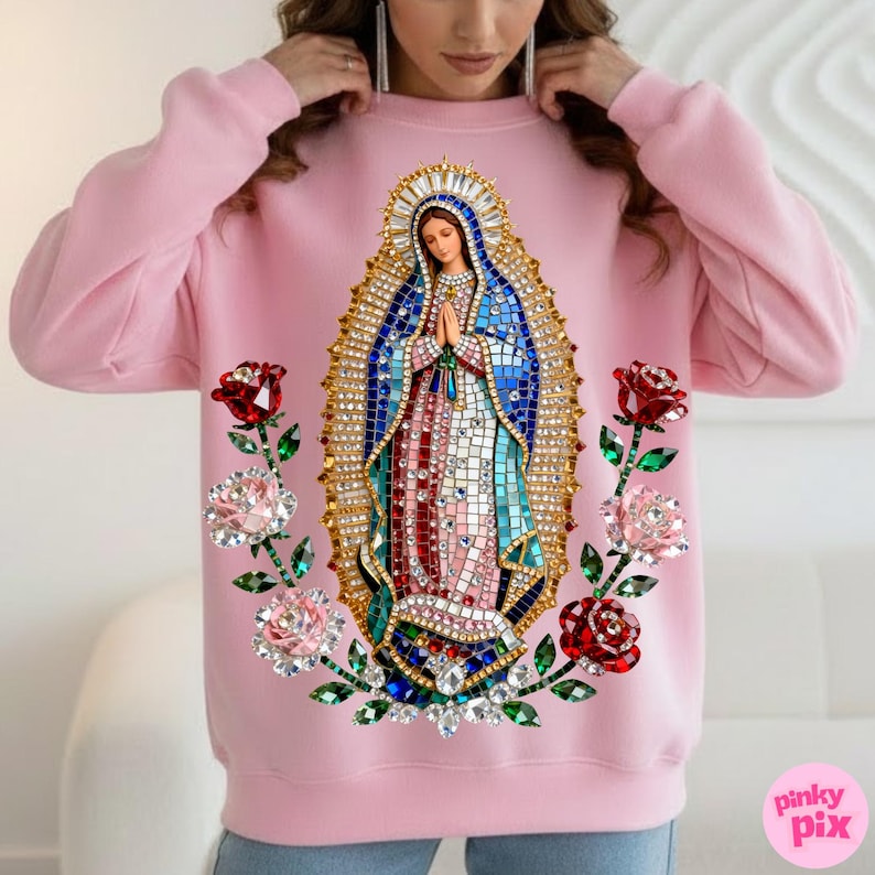 May include: A light pink sweatshirt featuring an image of the Virgin Mary with a jeweled halo and robe. The design includes red and pink roses with green stems and leaves. The sweatshirt has long sleeves and a crew neck.