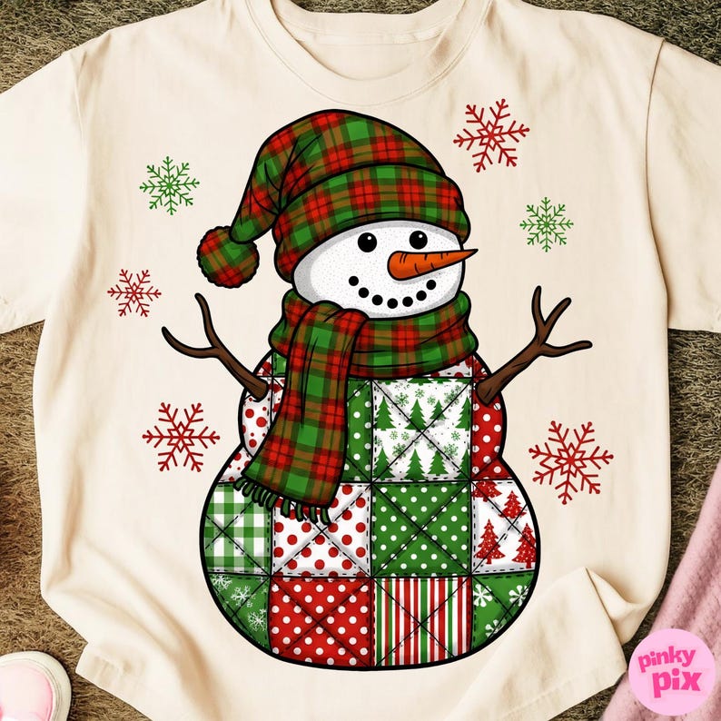 May include: Cream-colored t-shirt featuring a snowman design. The snowman has a plaid hat and scarf in red and green. The body is made of patchwork squares in red, green, and white. Brown twig arms and a carrot nose complete the design. Red and green snowflakes are scattered around the snowman.