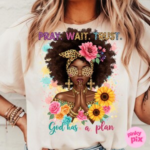 May include: A white t-shirt with a graphic design of a woman with a leopard print headband and sunglasses. The woman is praying with her hands clasped together. The text "Pray. Wait. Trust. God has a plan" is printed on the shirt.