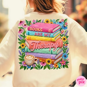 May include: Cream-colored sweatshirt featuring a colorful graphic of stacked books with the words "BOOKS ARE MY THERAPY." The design includes a coffee cup and floral accents in pink, yellow, blue, and purple.