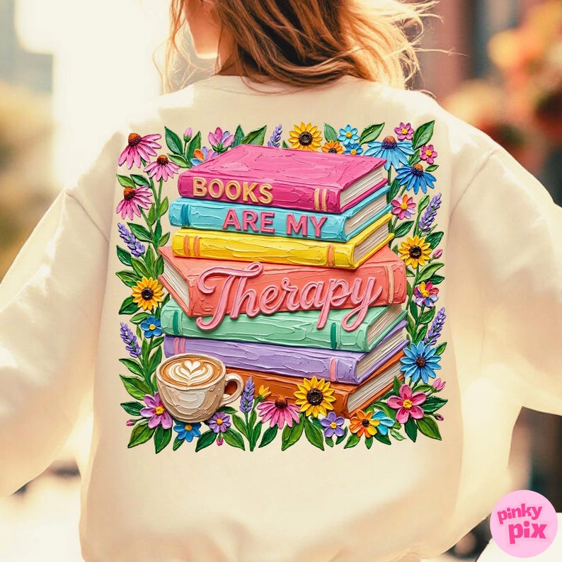 May include: Cream-colored sweatshirt featuring a colorful graphic of stacked books with the words "BOOKS ARE MY THERAPY." The design includes a coffee cup and floral accents in pink, yellow, blue, and purple.