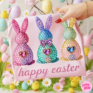 May include: A pink Easter-themed tote bag featuring three jeweled bunny designs in pink, blue, and yellow. Each bunny has a heart-shaped gem and the words "happy easter" in a sparkling font. The background includes Easter decorations.