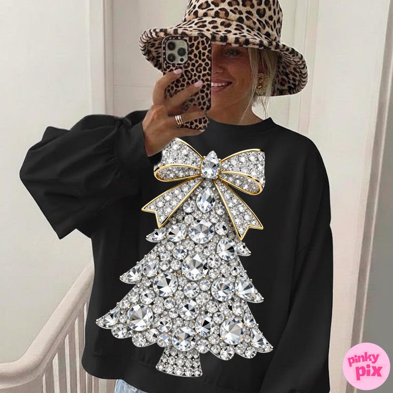 May include: Black sweatshirt featuring a sparkling Christmas tree design made of crystals and a gold bow. The sweatshirt has long sleeves and a crew neck. The image also shows a leopard print hat.