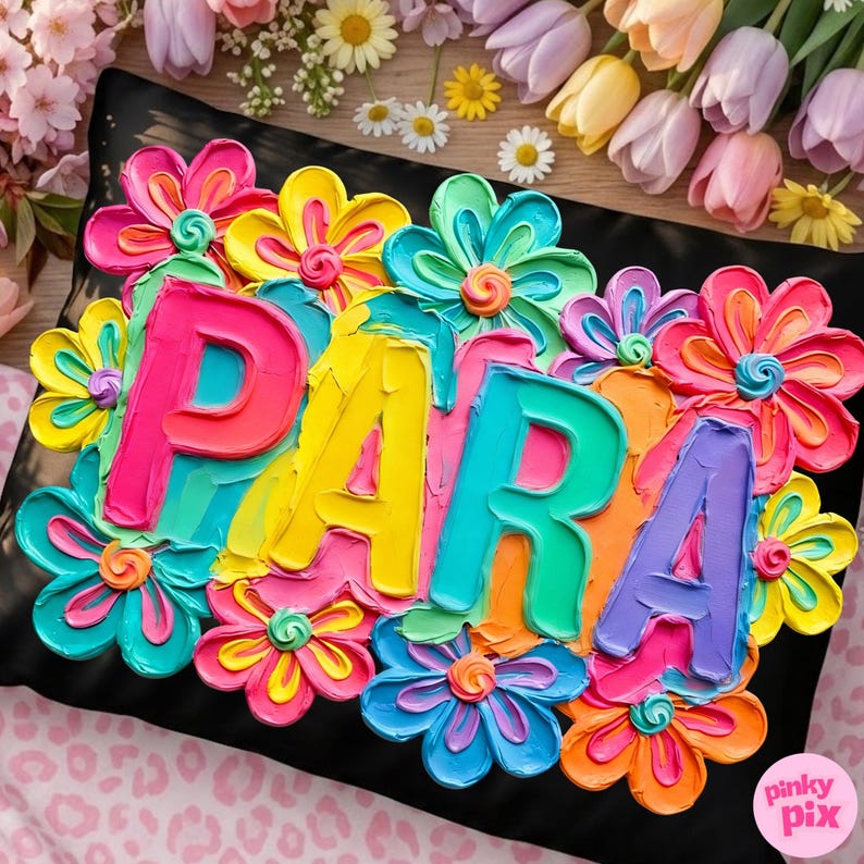 May include: A black pillow with the word "PARA" in colorful, textured letters, surrounded by vibrant, painted flowers in shades of pink, yellow, blue, and orange. The flowers have green centers. The pillow is decorated with a floral design.