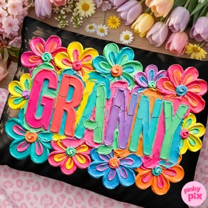 May include: Black pillow with the word "GRANNY" in colorful, textured letters, surrounded by vibrant, painted flowers in shades of pink, yellow, blue, and orange. The pillow has a textured, painted appearance, with a "pinky pix" logo in the bottom right corner.