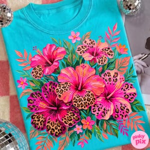 May include: A turquoise crew neck sweatshirt featuring a vibrant floral design. The design includes large pink hibiscus flowers with leopard print centers, surrounded by green leaves and smaller pink flowers. The brand name "pinky pix" is visible in the lower right corner.