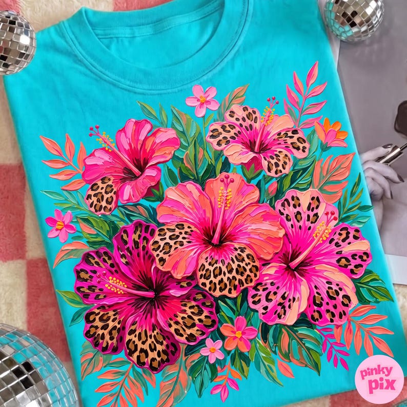 May include: A turquoise crew neck sweatshirt featuring a vibrant floral design. The design includes large pink hibiscus flowers with leopard print centers, surrounded by green leaves and smaller pink flowers. The brand name "pinky pix" is visible in the lower right corner.