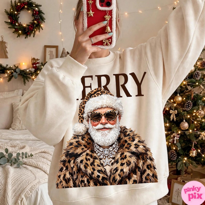 以下が含まれることがあります： クリーム色のクルーネックのスウェットシャツ。茶色の文字で「MERRY」と書かれ、その下にヒョウ柄のコート、お揃いのヒョウ柄の帽子、サングラス、大きなクリスタルのステートメントネックレスを身に着けたサンタクロースのグラフィックがプリントされています。