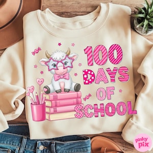 Pu&ograve; includere: Felpa color crema con una grafica raffigurante una mucca dei cartoni animati con occhiali a forma di stella e un papillon, seduta su libri rosa. Il testo "100 DAYS OF SCHOOL" &egrave; in rosa. &Egrave; presente anche un portapenne con matite a forma di cuore.