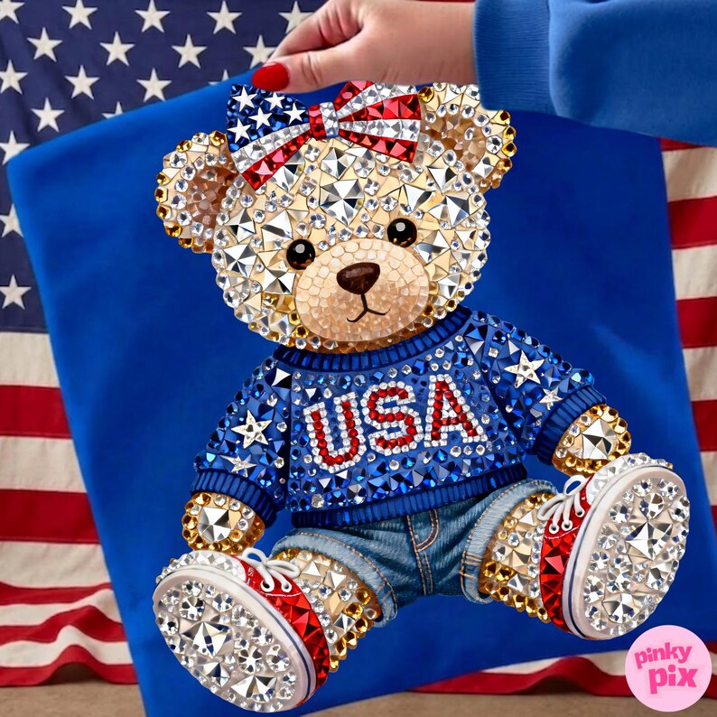 May include: A bedazzled teddy bear wearing a blue sweater with "USA" in red letters, denim shorts, and red, white, and blue sneakers. The bear has a bow with stars and stripes. The background includes a blue fabric and an American flag.