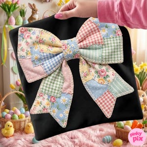 Może przedstawiać: Czarna poduszka z dużą patchworkową kokardą. Kokarda ma różne pastelowe tkaniny z kwiatowymi, kratkowanymi i groszkowymi wzorami. Kokarda jest punktem centralnym, z ręką trzymającą poduszkę w tle.